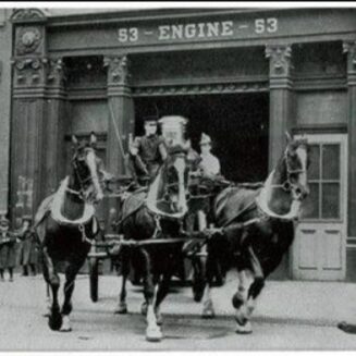 A horse-drawn fire engine leaving a fire house.